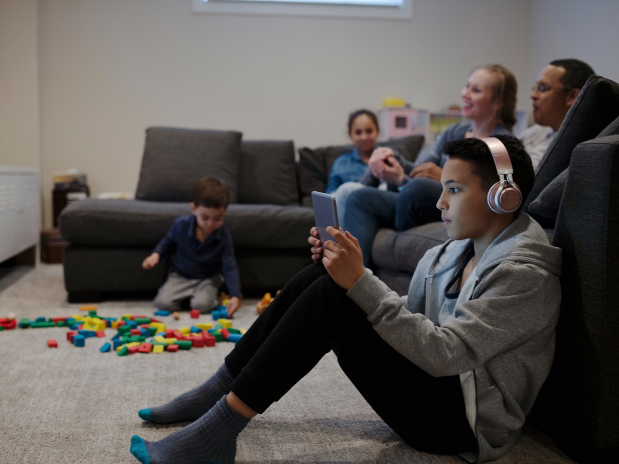 Family at home watching TV, child watching Ipad with headphones.